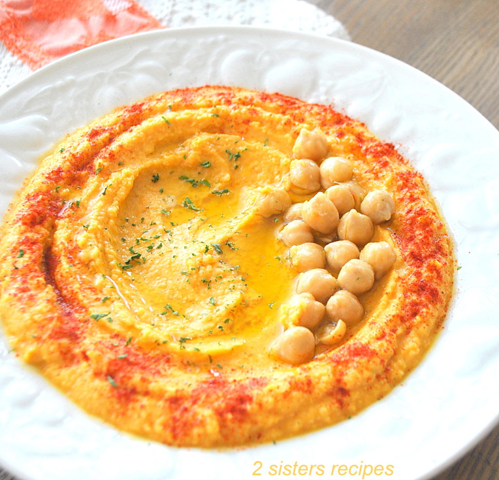 A white plate filled with creamy chickpea hummus topped with paprika and some chickpeas.