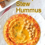 A white plate filled with a creamy chickpea hummus topped with some chickpeas and paprika.