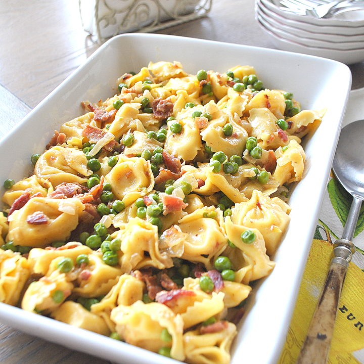 In a white baking dish filled with tortellini pasta, peas and bacon.