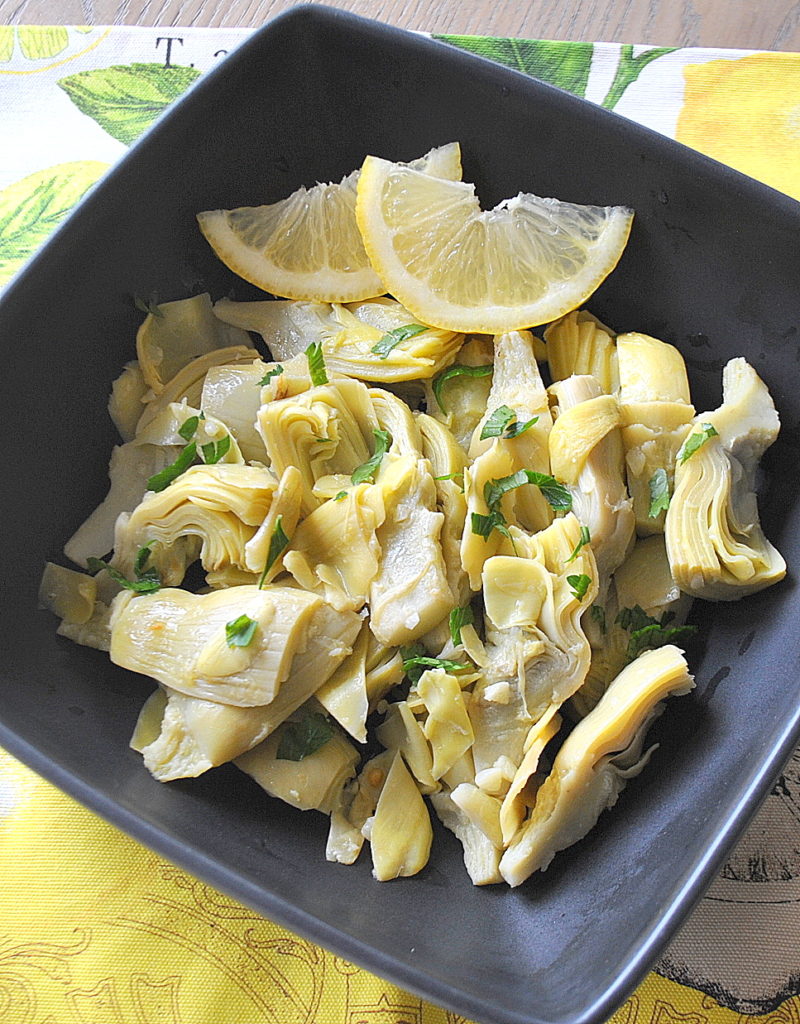A square bowl filled with artichoke hearts and lemon slices.