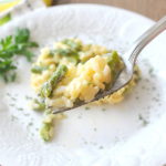 A forkful of risotto with asparagus over a white plate.