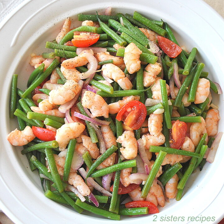 A white round salad bowl filled with cooked green beans, shrimp and cherry tomatoes.