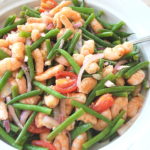 A white salad bowl filled with cooked shrimp, green beans and cherry tomatoes.