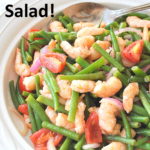 A white salad bowl filled with cooked green beans, shrimp and cherry tomatoes.