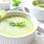 A white ramekin filled with a light green colored soup topped with fresh mint leaf.