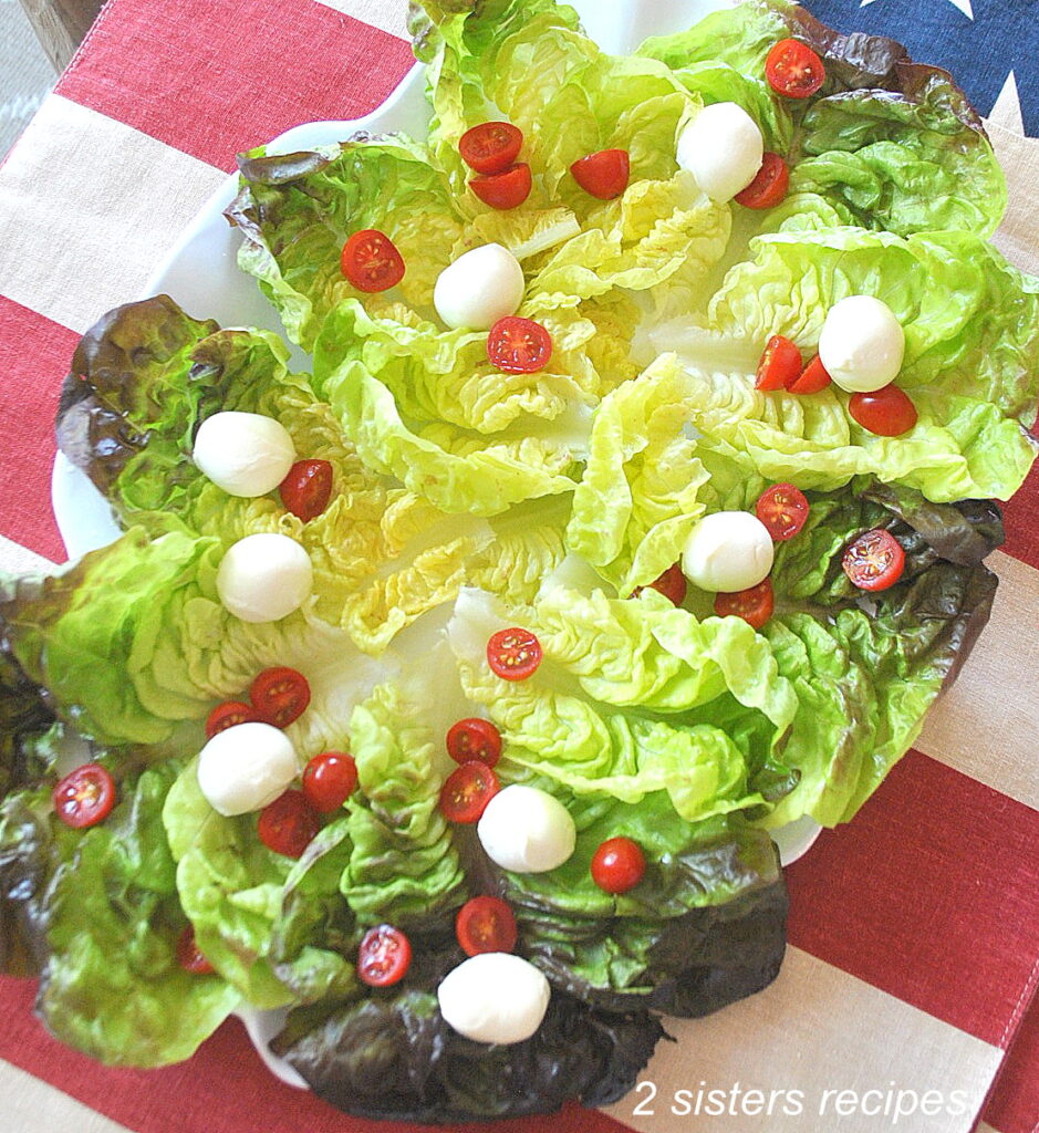A platter filled with red leaf lettuce topped with cherry tomatoes and small cheese balls.