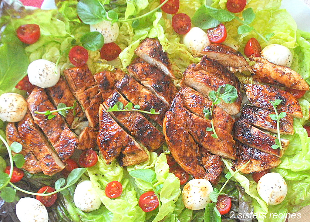 A sliced grilled chicken served on a bed of lettuce with cherry tomatoes and small mozzarella balls.