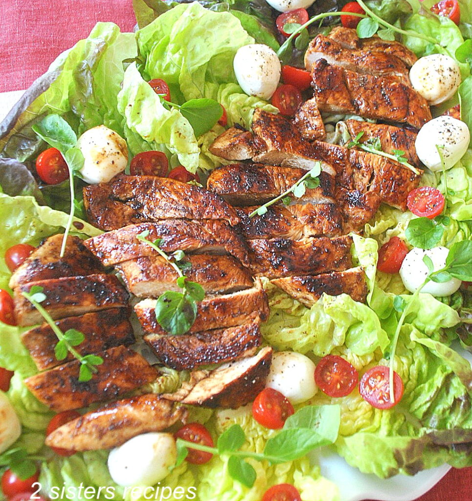 A sliced grilled chicken served on a bed of lettuce with cherry tomatoes and small mozzarella balls.