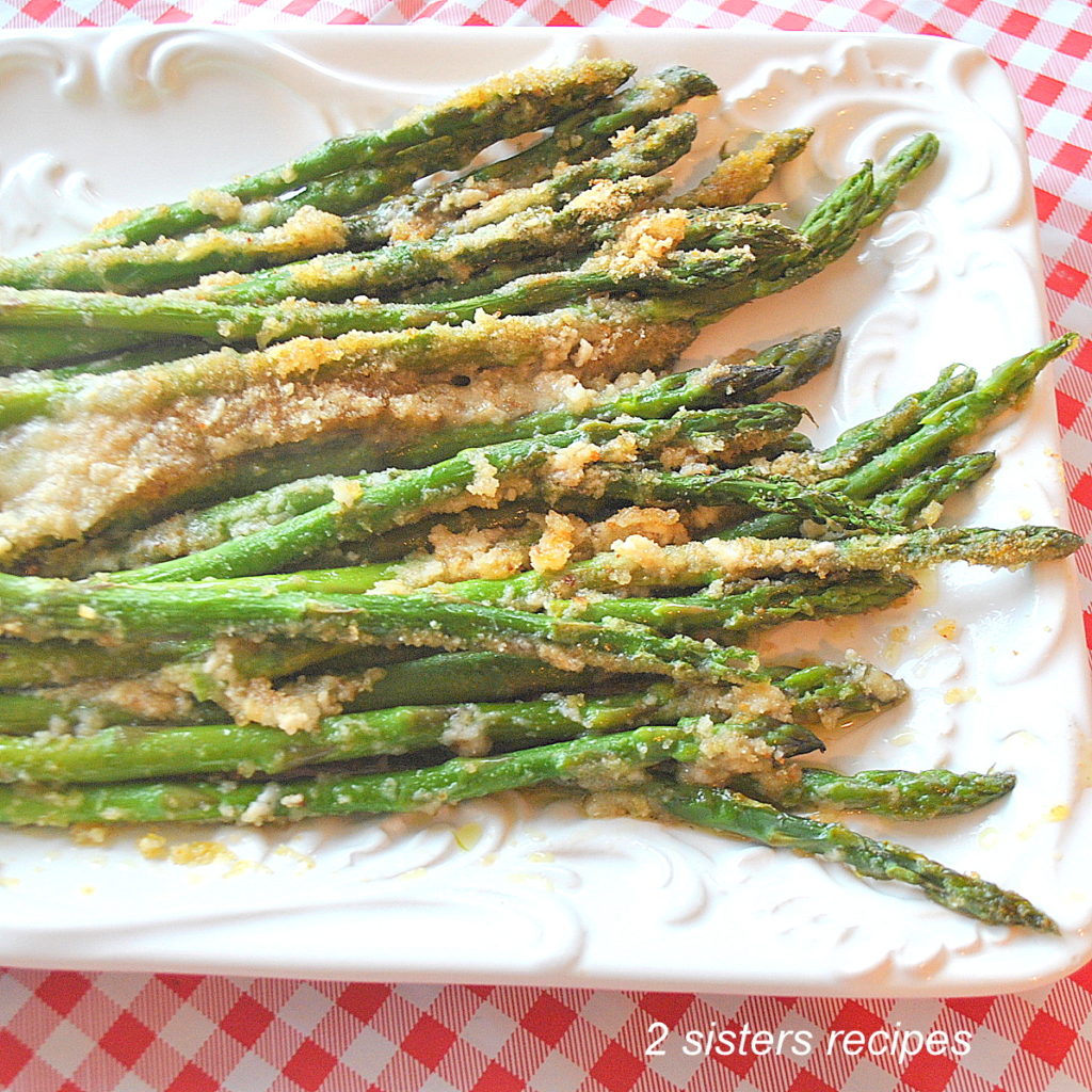Baked asparagus topped with bread crumbs is served on a white platter.