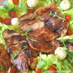 A grilled sliced chicken is served on a bed of lettuce with sliced tomatoes and mozzarella cheese balls.