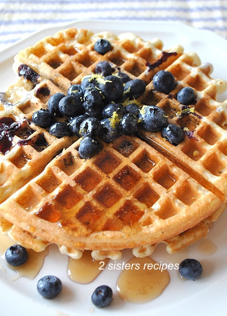 A white plate filled with waffle topped with fresh blueberries and maple syrup.
