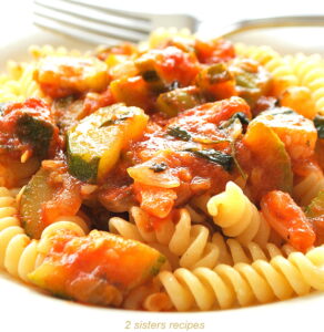 A plate filled with fusilli pasta topped with tomato and zucchini sauce.