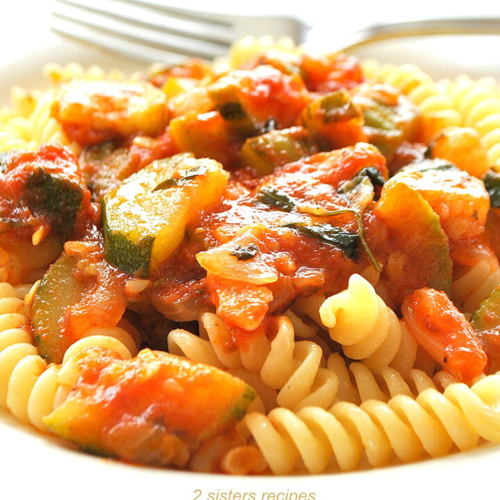 A plate filled with fusilli pasta topped with tomato and zucchini sauce.