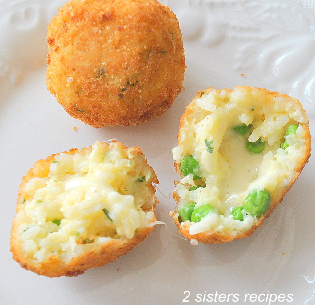 Two rice balls on a white plate with one rice ball open to see the baby peas inside.