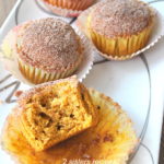 Pumpkin muffins served on a white and silver platter, with a bite into one muffin.