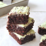 A pile of chocolate chip brownies topped with green mint icing on a sheet of wax paper