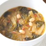 A white bowl filled with a soup made with white beans and escarole.