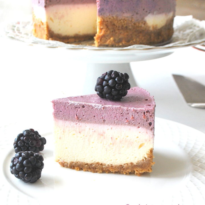 A slice of double layer cheesecake with a blackberry layer on top served on a white plate.