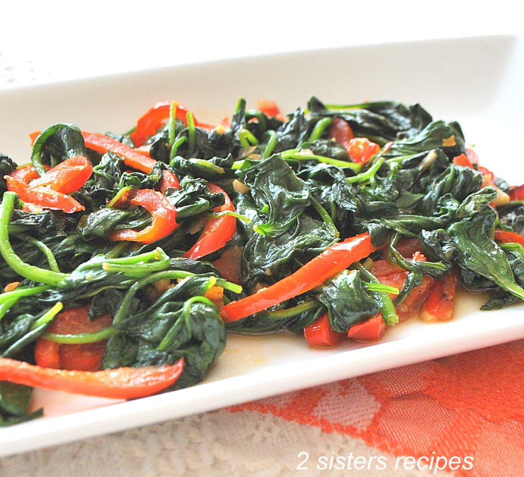 A white platter filled with spinach and red peppers.