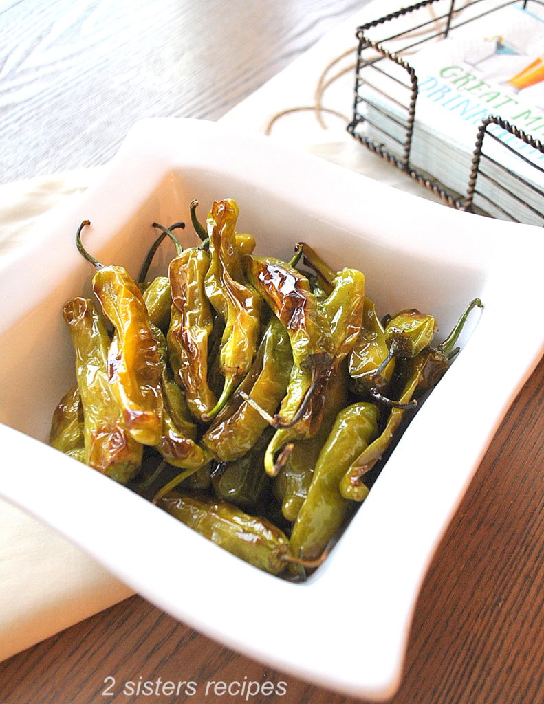 white square bowl filled with baked shishito peppers.