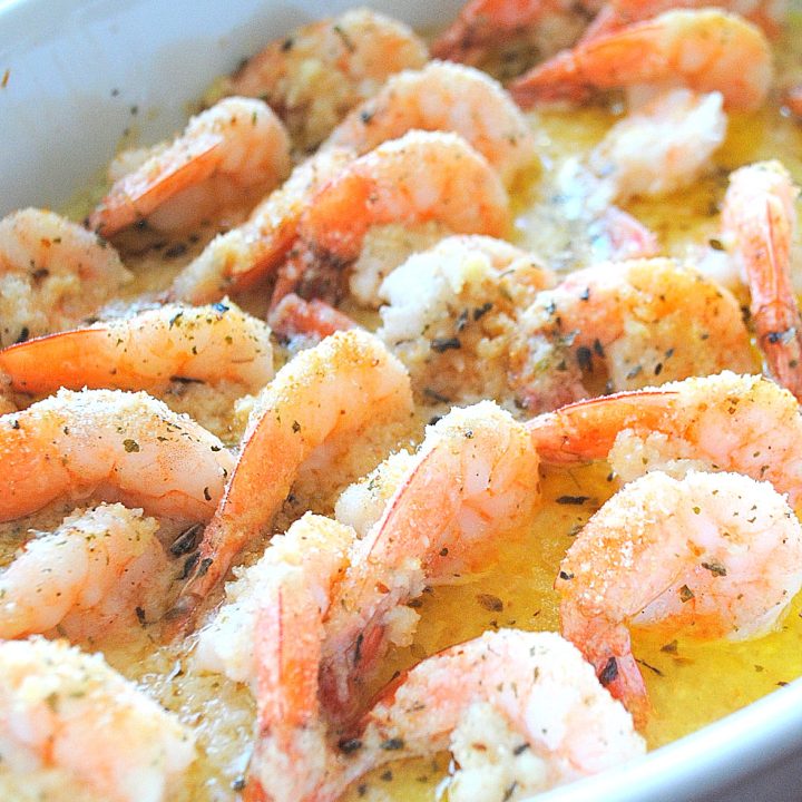 A white baking dish filled with cooked shrimp in a lemon sauce.