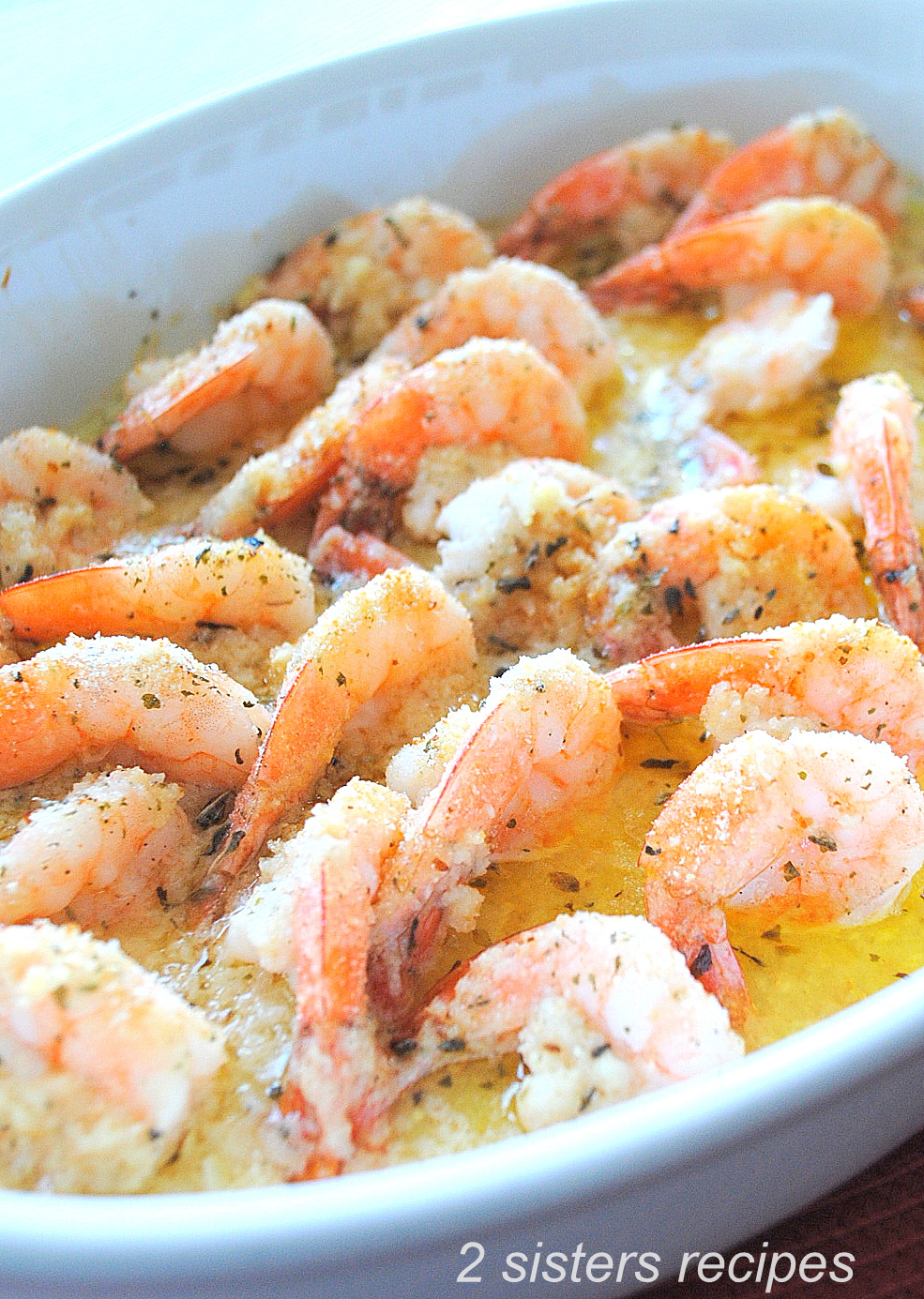 A white baking dish filled with cooked shrimp in a lemon sauce.