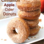 A pile of apple cider donuts coated with cinnamon sugar on a white platter.