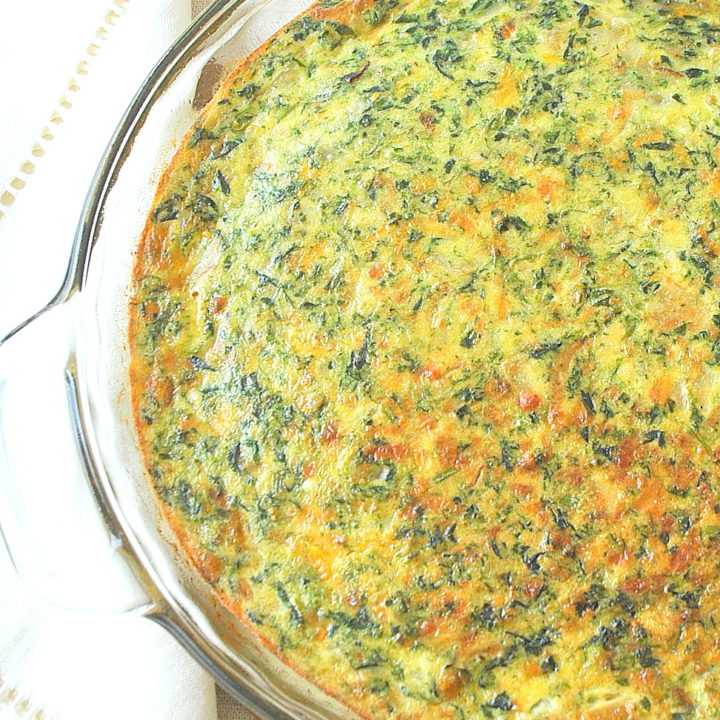 A glass baking dish with a baked crustless quiche filled with spinach and cheese.