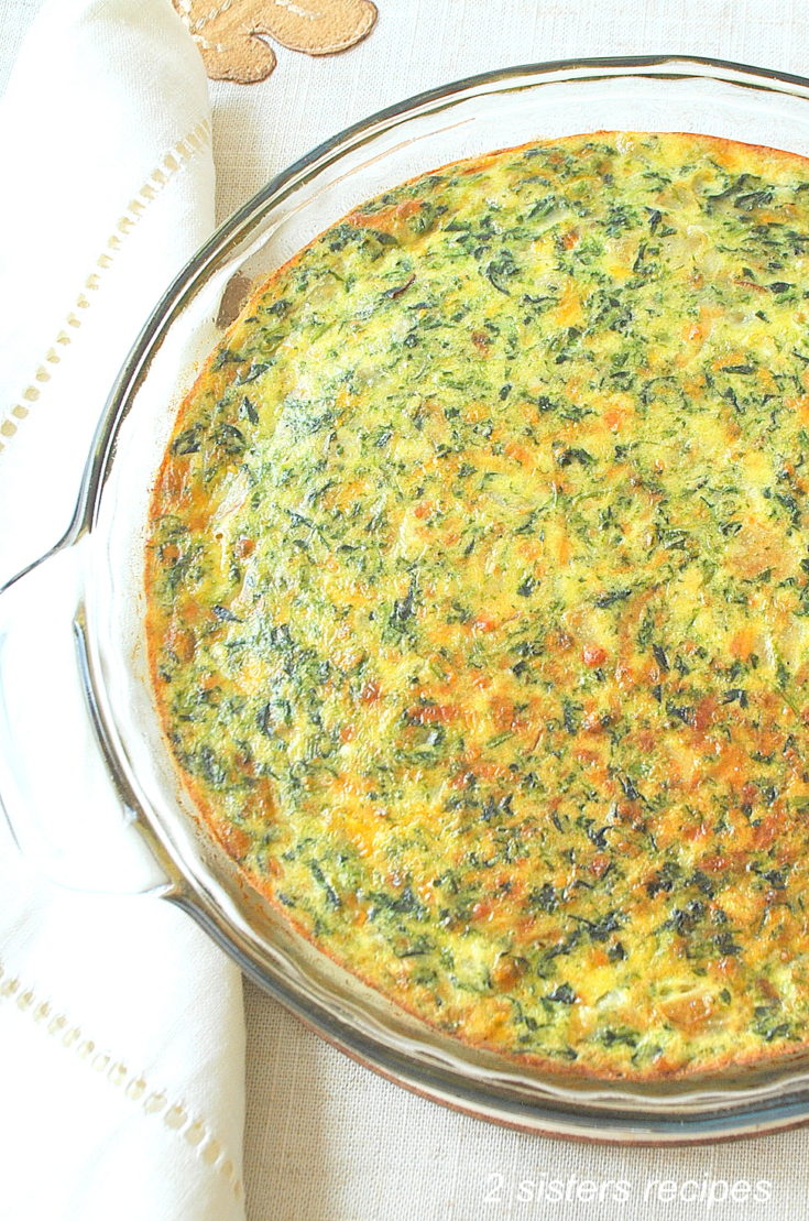 A glass baking dish with a baked crustless quiche filled with spinach and cheese.