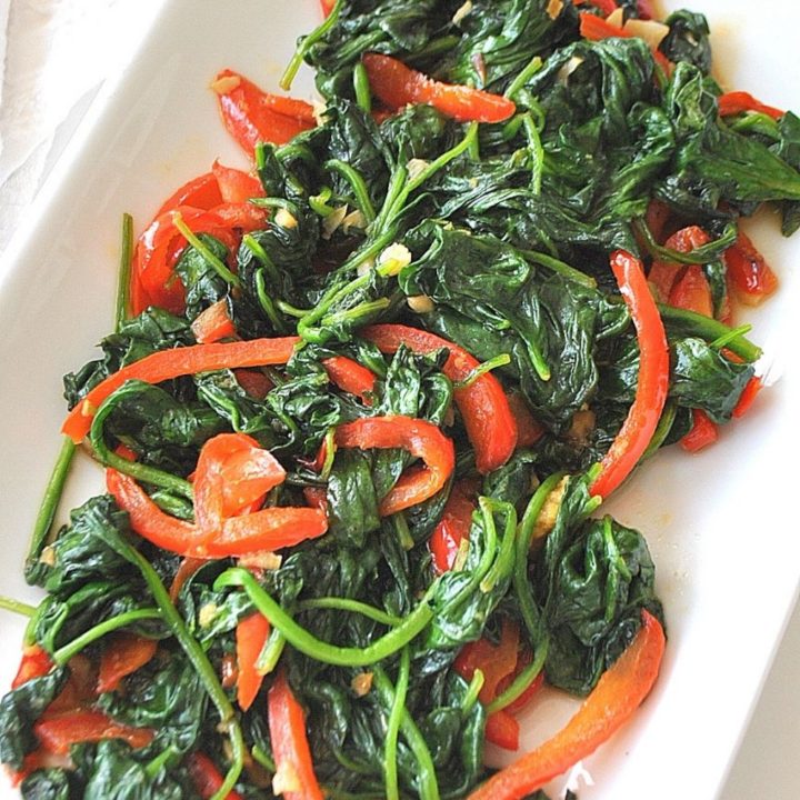 A white platter filled with cooked spinach and sliced red peppers.