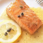 A serving of cooked salmon with lemon sauce and topped with capers.
