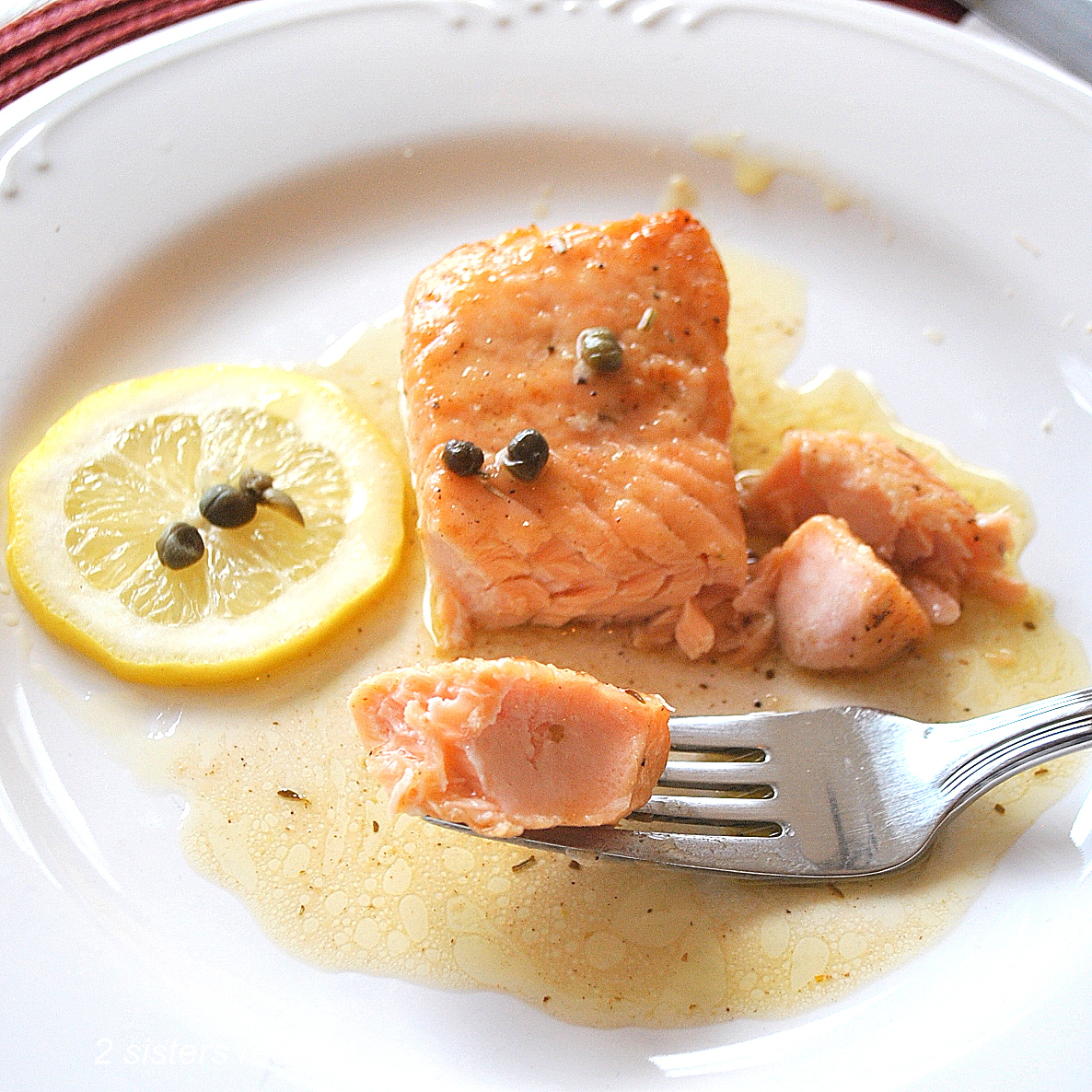 A white plate with a serving of salmon piccata and a forkful of salmon.