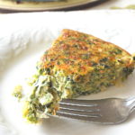 A forkful of spinach and cheese filled quiche on a white plate.
