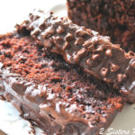 A chocolate bread, topped with chocolate ganache and mini chips is sliced on a white platter.