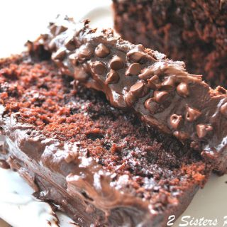 A chocolate bread, topped with chocolate ganache and mini chips is sliced on a white platter.