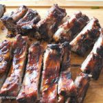 A wood cutting board with sliced roasted baby back ribs.