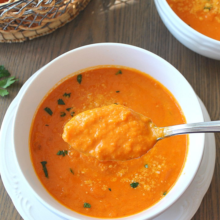 A spoonful of tomato soup over a white bowl.