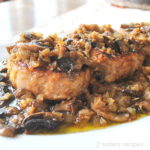 Three cooked pork chops topped with a mushroom and onion sauce, served on a white platter.
