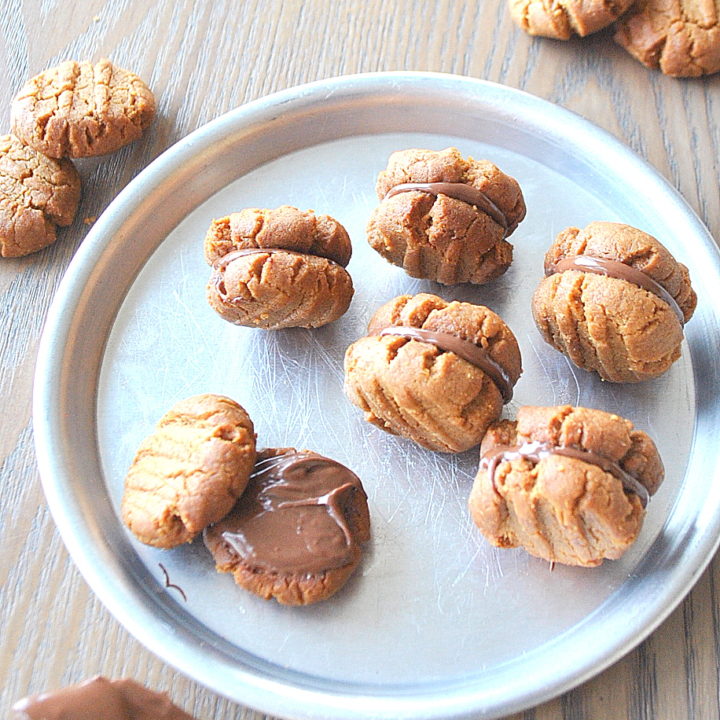 A silver plate filled with mini peanut butter cookies filled with chocolate filling. by 2sistersrecipes.com