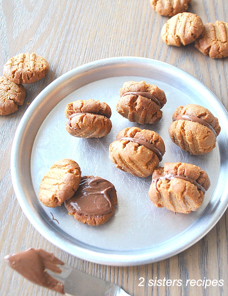 A silver plate filled with mini peanut butter cookies filled with chocolate filling. by 2sistersrecipes.com