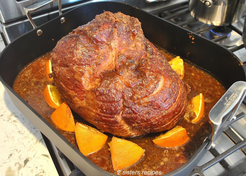 Fully cooked ham with oranges slices around is pulled out of from the oven.