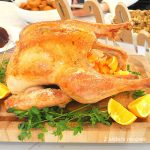 A full roasted turkey sitting on a wood cutting board with sliced oranges on the side.