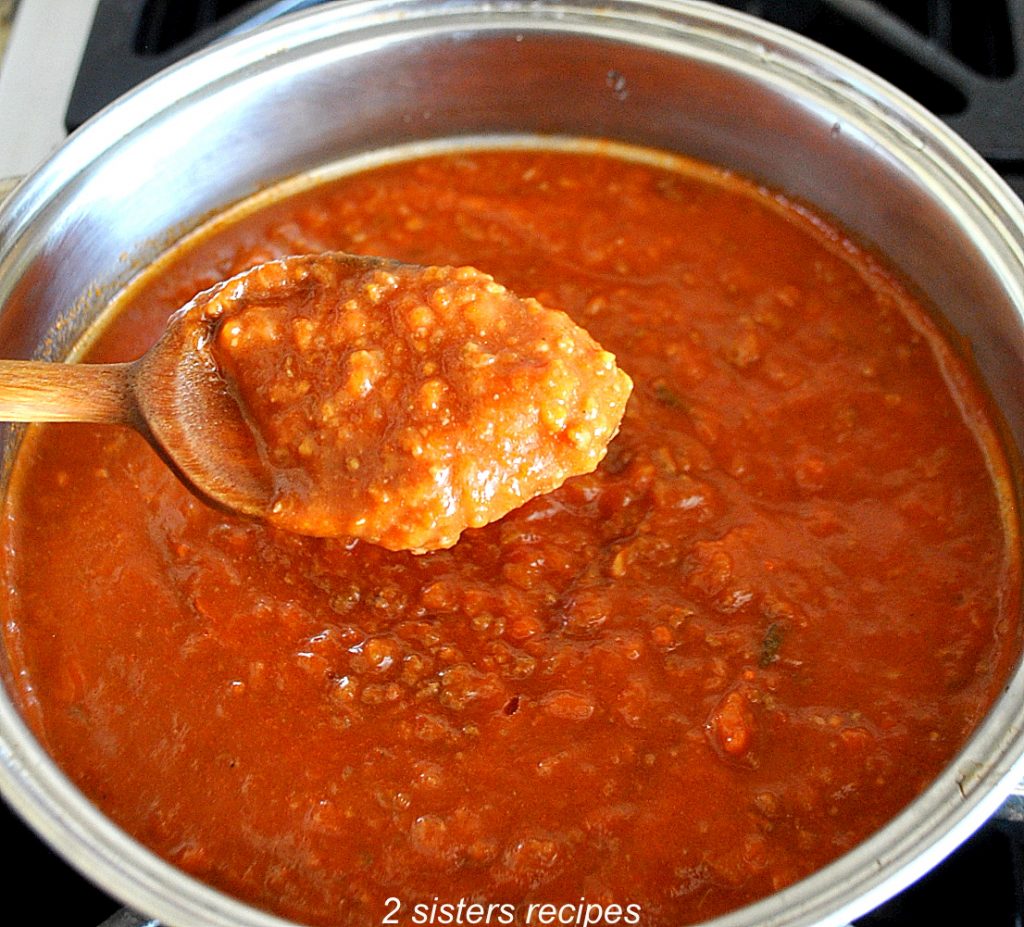 A wooden spoon full of mom's classic Bolognese sauce over the pot. 