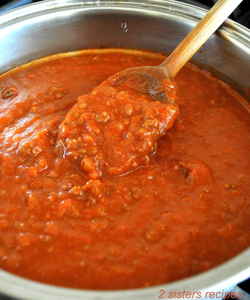 A wooden spoon filled with a thick tomato sauce inside a pot on stove top.