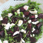 A white platter with arugula, chopped beets and goat cheese salad.