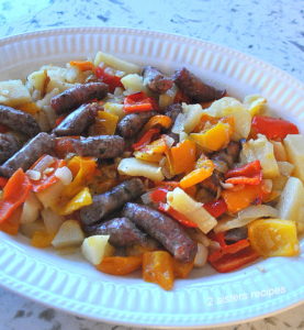 A large white platter filled with baked sausages, peppers and potatoes.