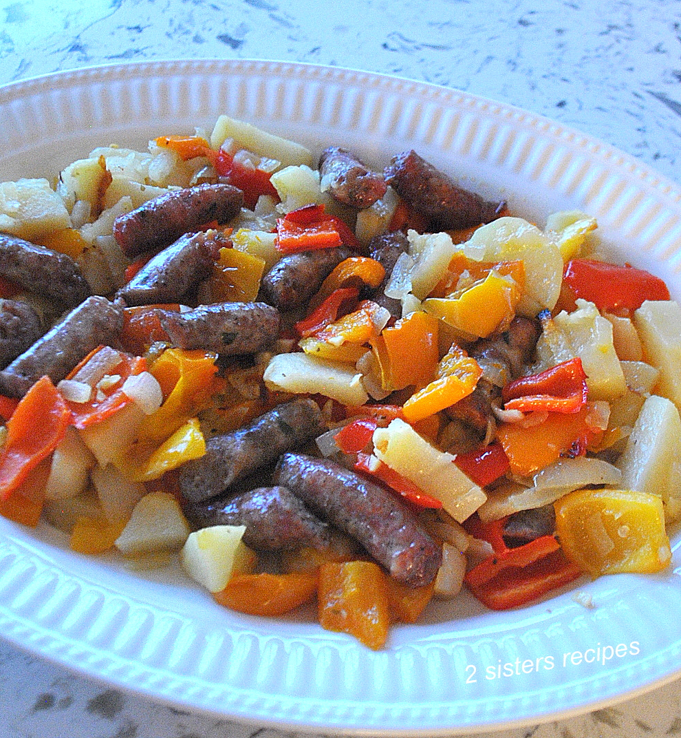A large white platter filled with baked sausages, peppers and potatoes.