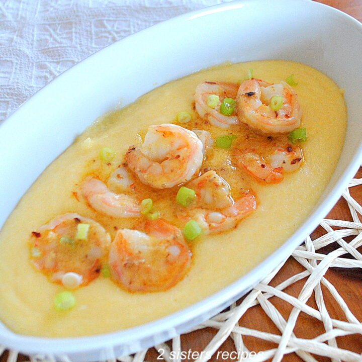 A white oval platter filled with polenta with shrimp laid on top.