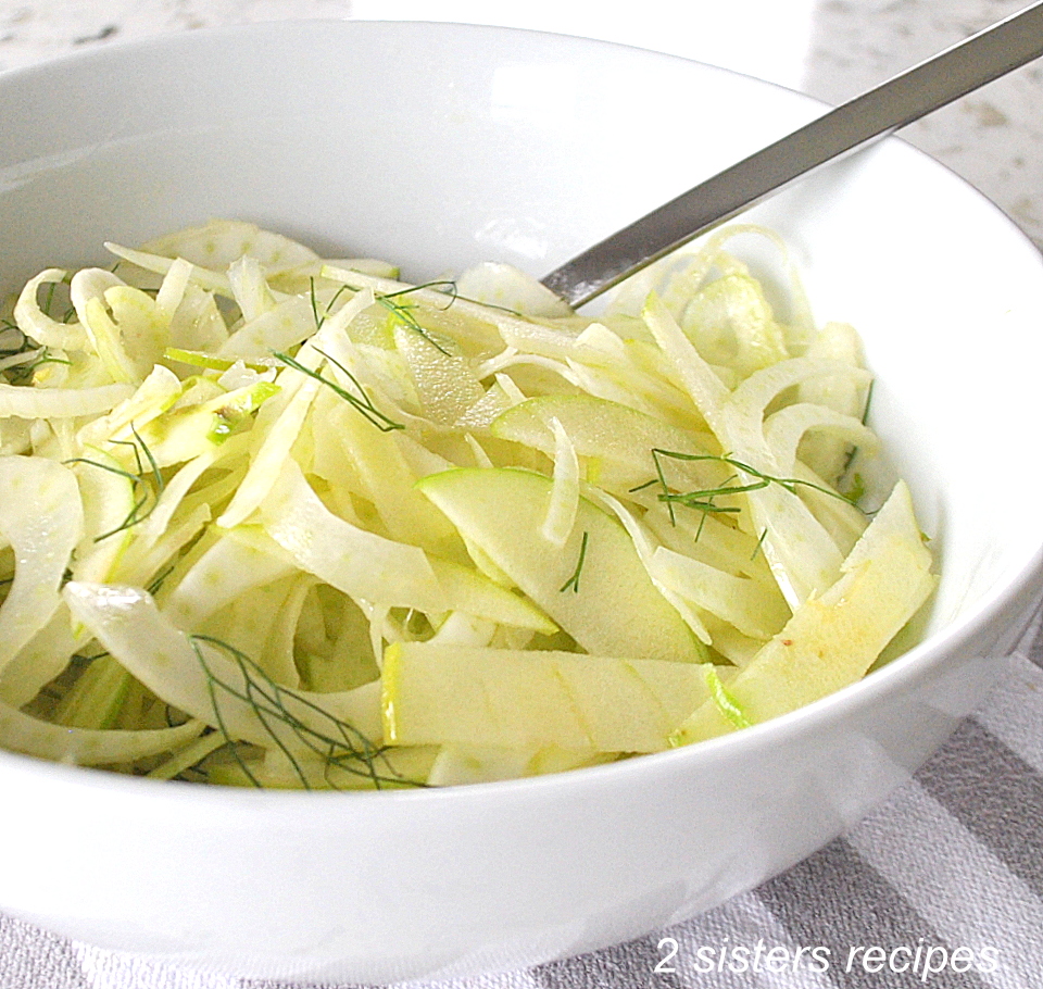 A white salad bowl filled with shavings of apples and fennel with a spoon.