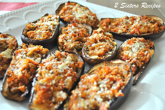 Eggplants sliced open and filled with vegetables and baked, served on a white platter.